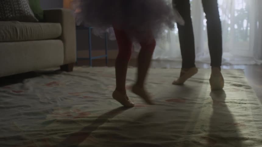 A girl in a ballerina outfit is dancing with a parent