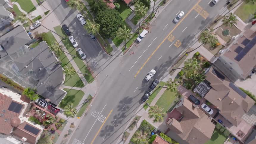 An aerial top-down view slowly descends and rotates over a residential neighborhood street intersection in a sunny suburb