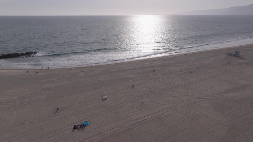 An expansive aerial shot slowly reveals a serene beach coastline with the sun setting over the tranquil ocean
