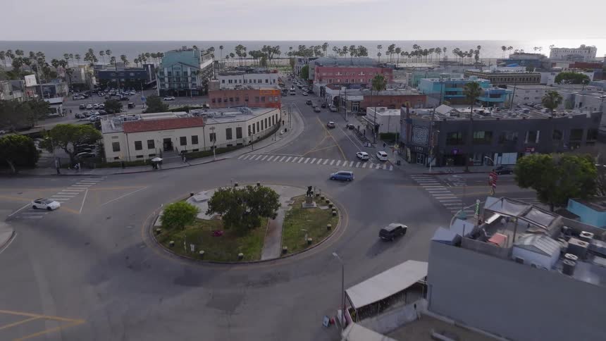 An aerial view pushes in from a residential street towards the iconic traffic circle and boardwalk of Venice Beach, California