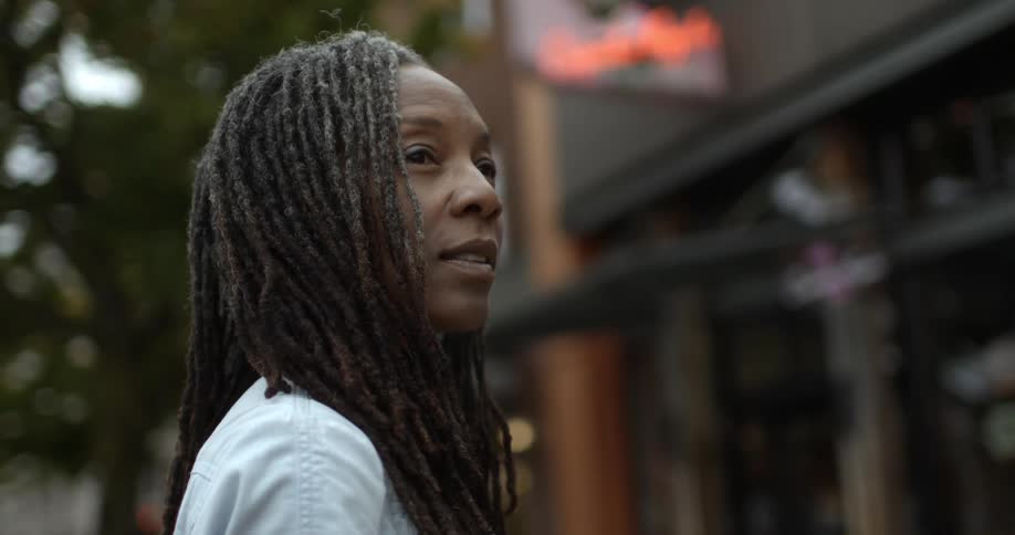 A woman stands in an urban setting and looks around her
