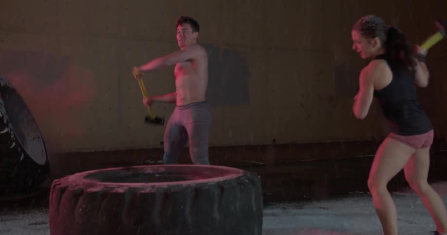 People hit a large tire with sledgehammers while it snows