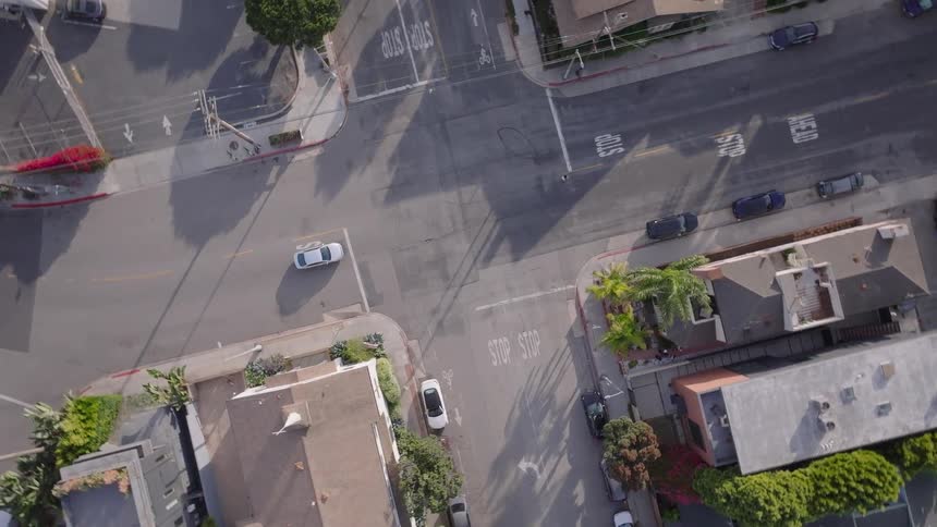 A slow-descending drone shot with a rotating camera captures a top-down view of a quiet street intersection in a residential area