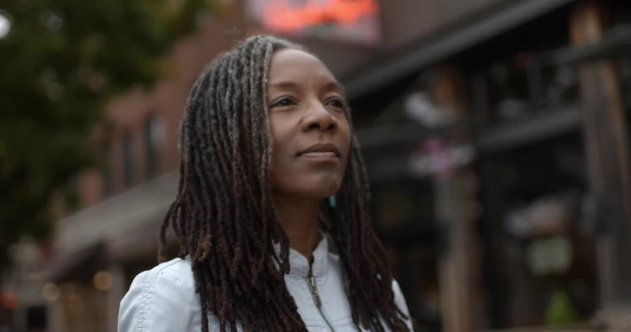A woman stands in an urban setting and stares straight ahead