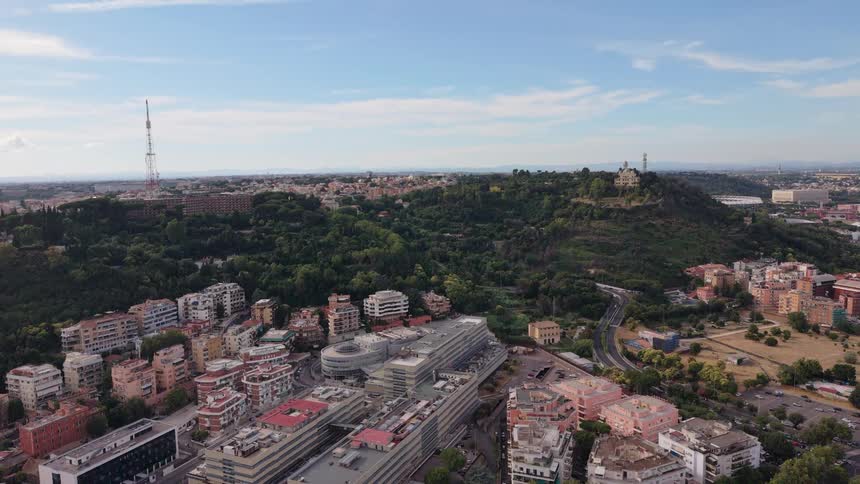 A slow pulling back aerial shot reveals a vast European cityscape with modern buildings and a prominent green hill on a sunny day