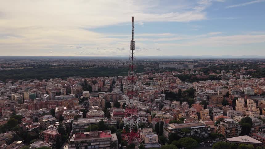 A striking aerial shot reveals a large telecommunications tower standing amidst the cityscape of Rome, Italy