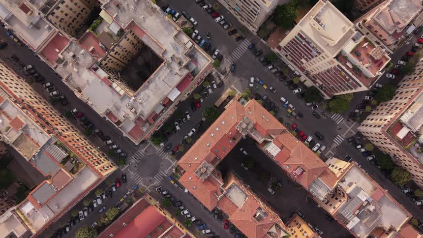 A slow ascending top-down aerial view of a classic European city intersection with apartment buildings and streets lined with parked cars