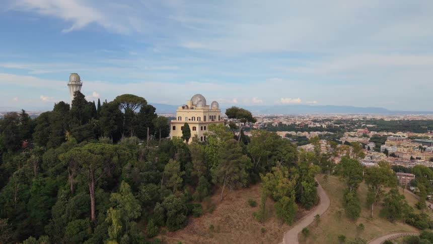 Scenic aerial fly-in shot of the Astronomical Observatory of Rome on a lush green hill overlooking the cityscape