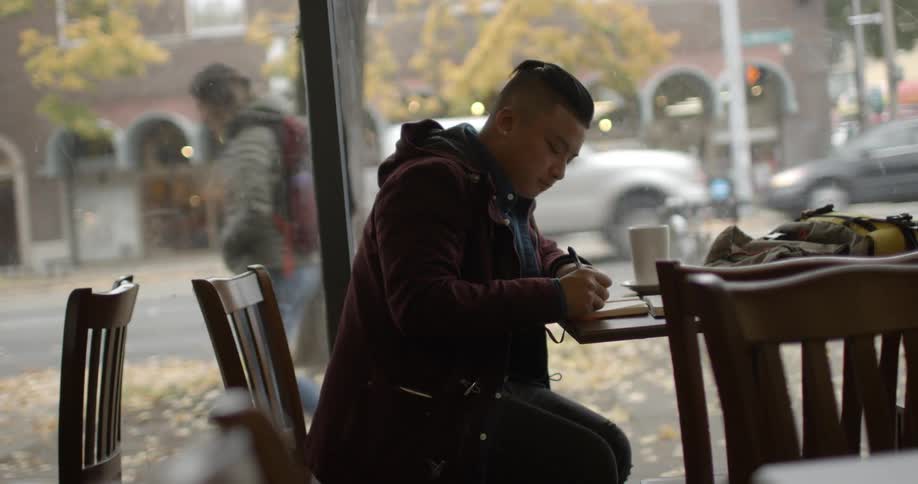 A man sits in a restaurant writing in a book