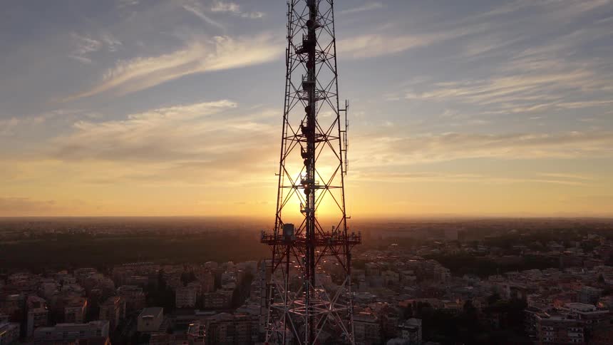 Aerial view of a telecommunication tower silhouetted against the vibrant sunset sky above a sprawling city