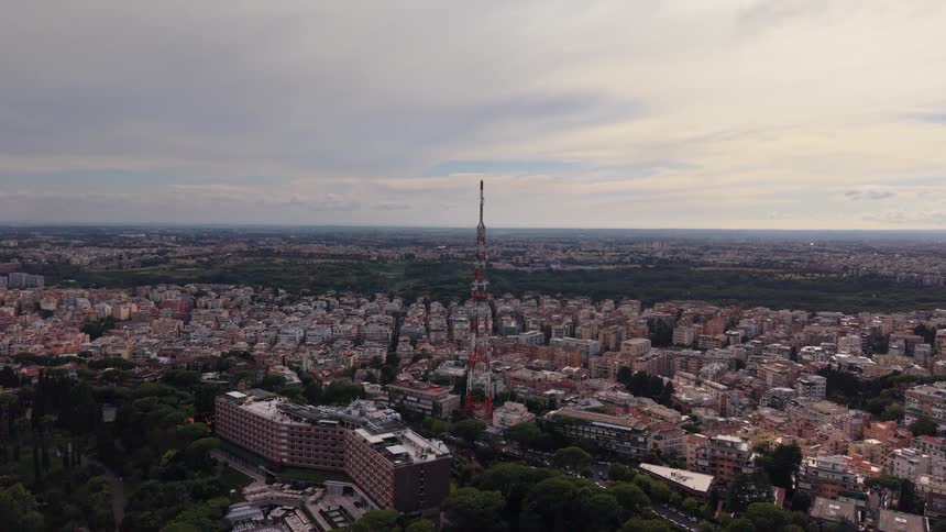 Static aerial perspective of a vast city skyline centered on a towering red and white broadcast antenna under an overcast sky