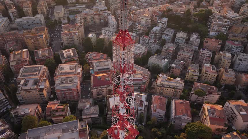 Aerial view of a tall communications tower at sunset, with the camera tilting down to reveal the sprawling city below