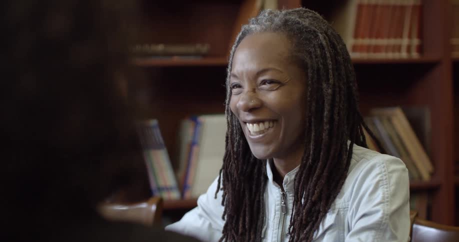 A woman in a library laughs while talking to someone