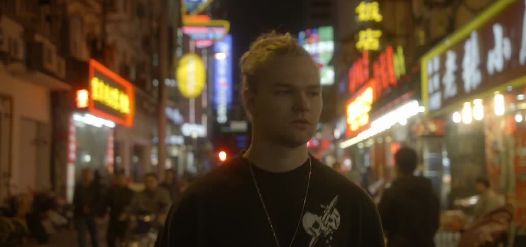 A young man walks down a busy asian street at night