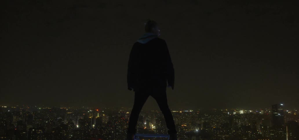 A man balances on a ledge overlooking a city at night