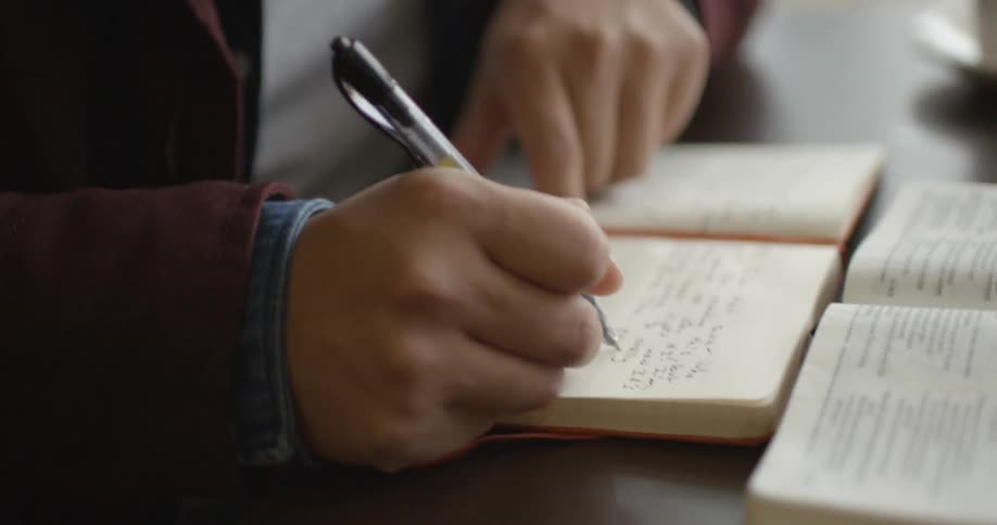Closeup of a person writing in a book with a pen