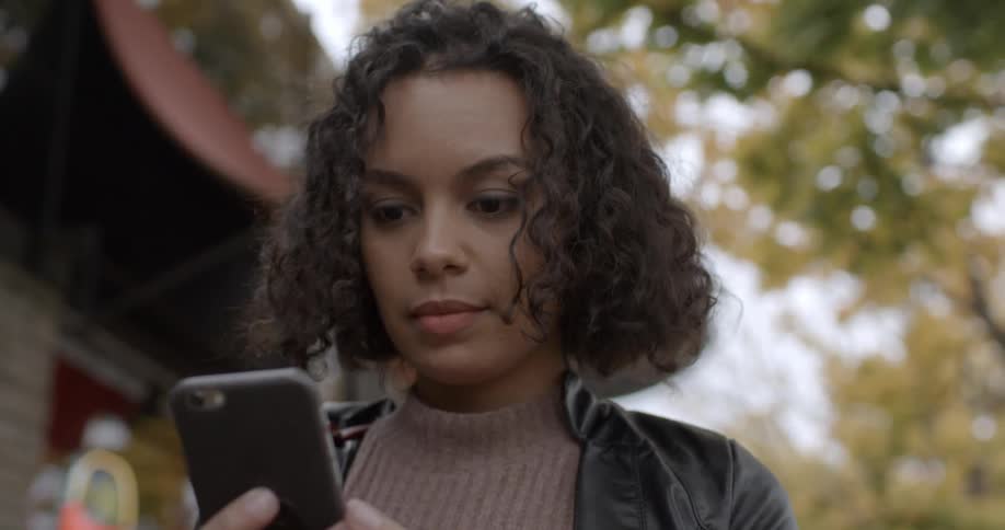 A woman is standing outside during the day looking at her phone