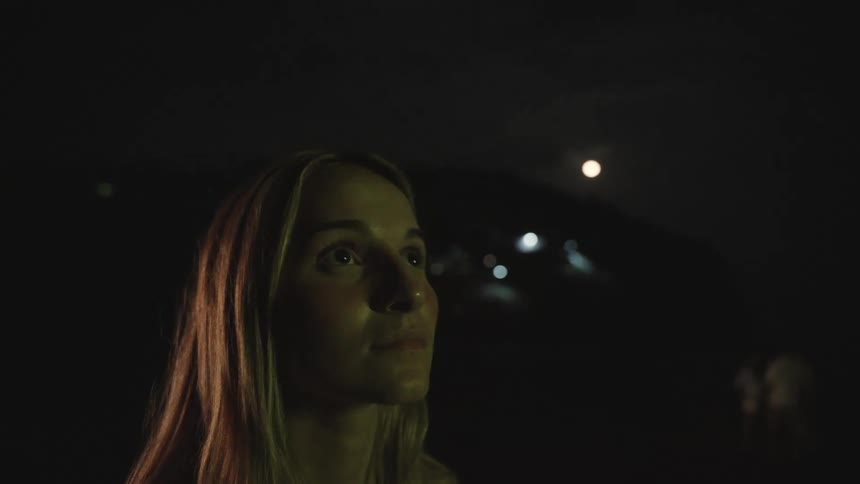 A young woman's face reflects colorful lights as she watches a spectacular event at night with a smile
