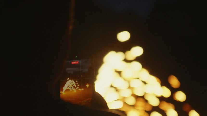 Over-the-shoulder view of a person filming a sparkling fire display with a smartphone at night