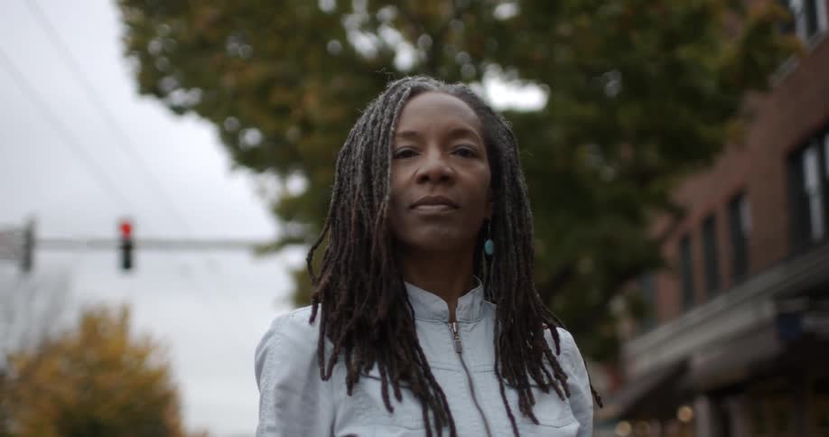 A black female stands staring forward on a city street