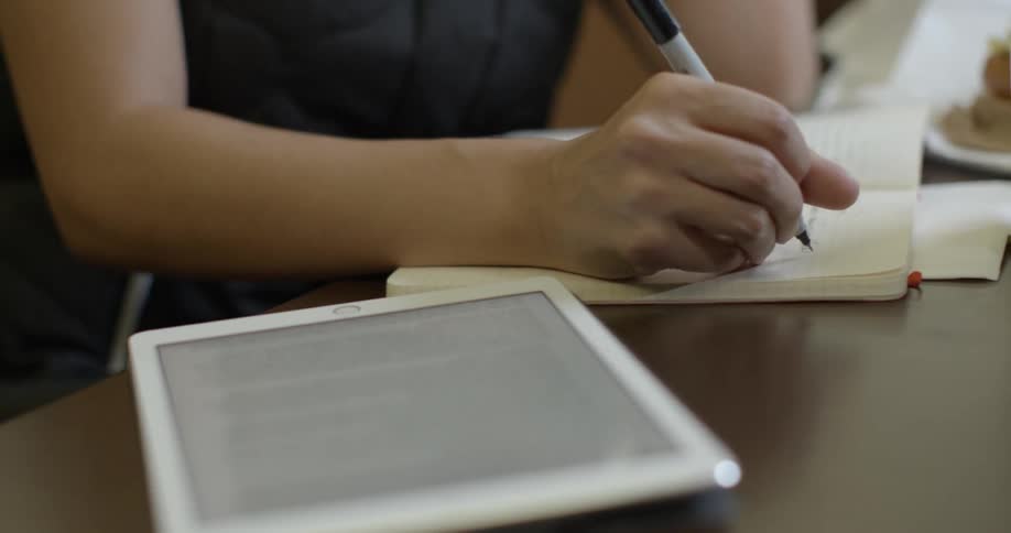 A woman is writing with a tablet nearby