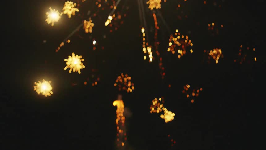 A person lights a firework rocket that launches into the night sky and explodes in a dazzling display of lights and sparks
