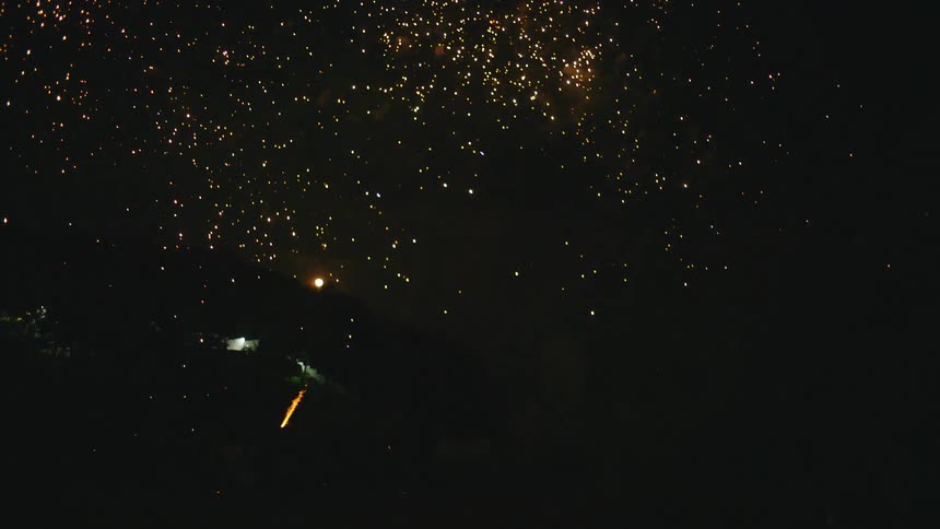 A group of friends celebrate on a dark tropical beach at night with a spectacular display of colorful fireworks exploding in the sky