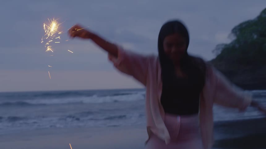 A man and woman celebrate by lighting sparklers and dancing joyfully on the beach at twilight