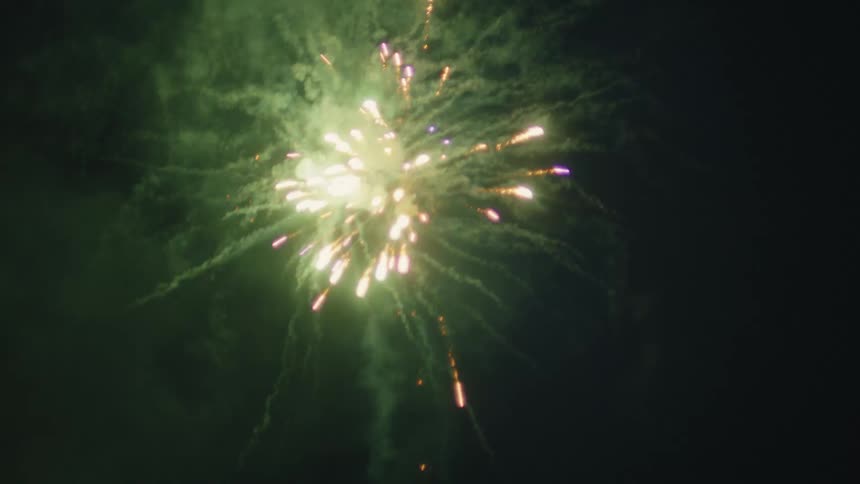 A slow-motion close-up captures a vibrant display of multicolored fireworks exploding in the dark night sky