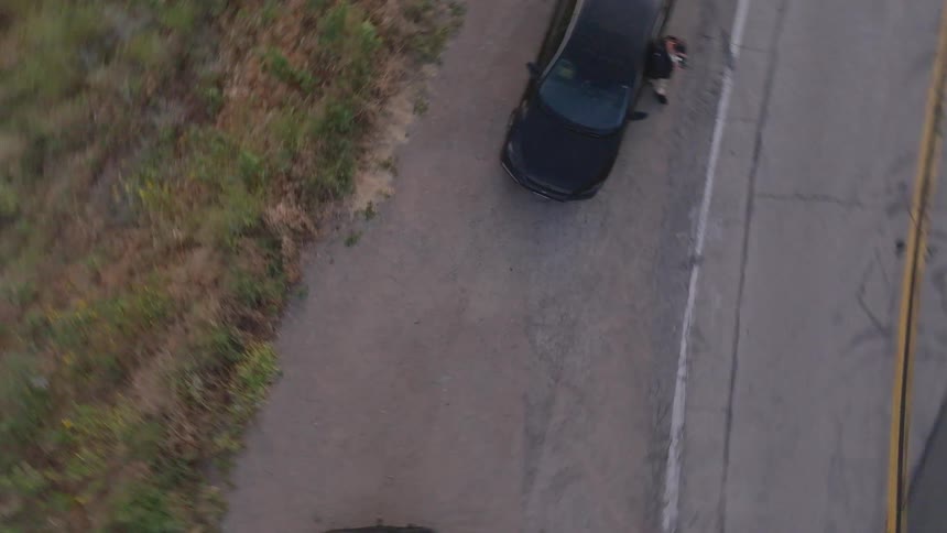 A top-down aerial drone shot rapidly spins and descends toward cars parked on the shoulder of a rural road