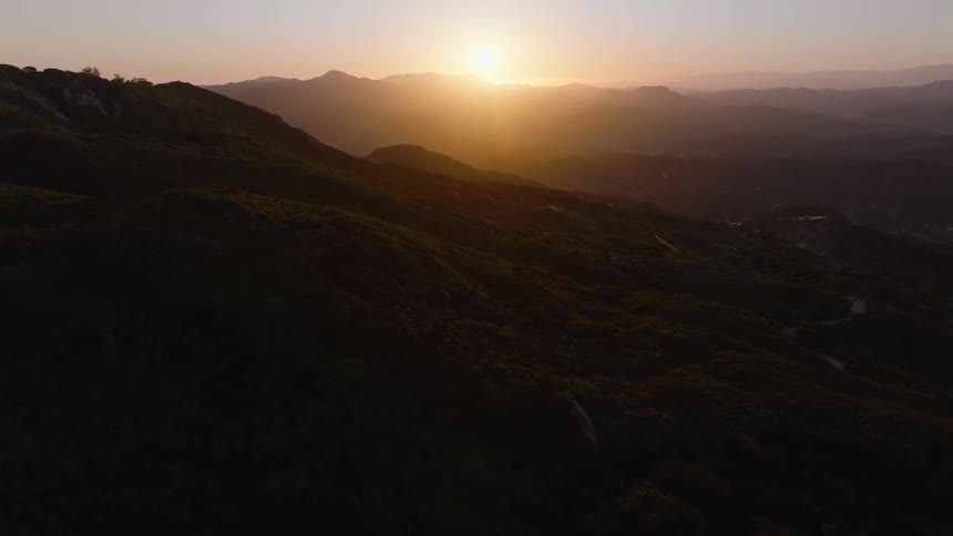 A breathtaking aerial shot captures the golden sun setting over a majestic and sprawling mountain landscape