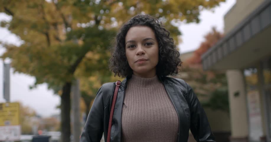A woman smiles and turns forward on the sidewalk