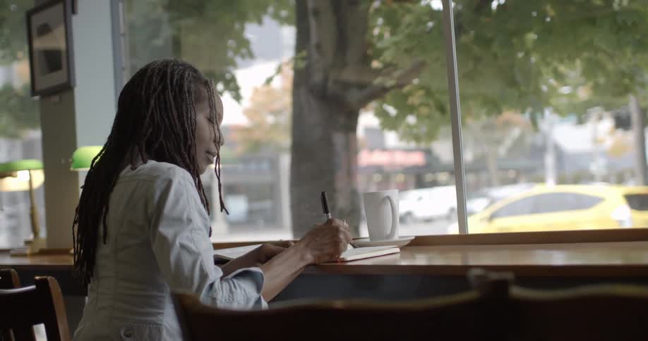 A woman writing in a book while sitting at a table inside