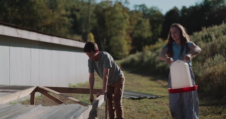 A brother and sister work together doing their farm chores, feeding and watering the chickens in slow motion