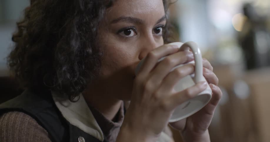 A woman drinks from a cup and interacts with another person