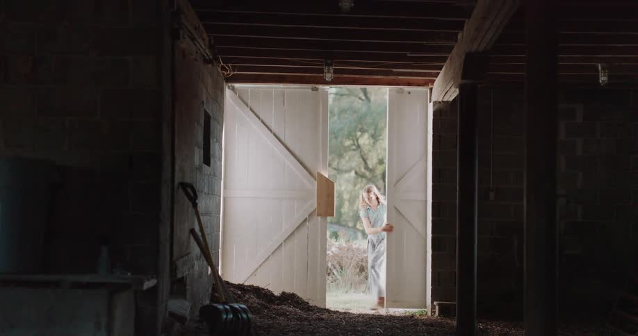 Silhouetted figures of a boy and a woman walk out of a dark, rustic barn and close the large white wooden doors