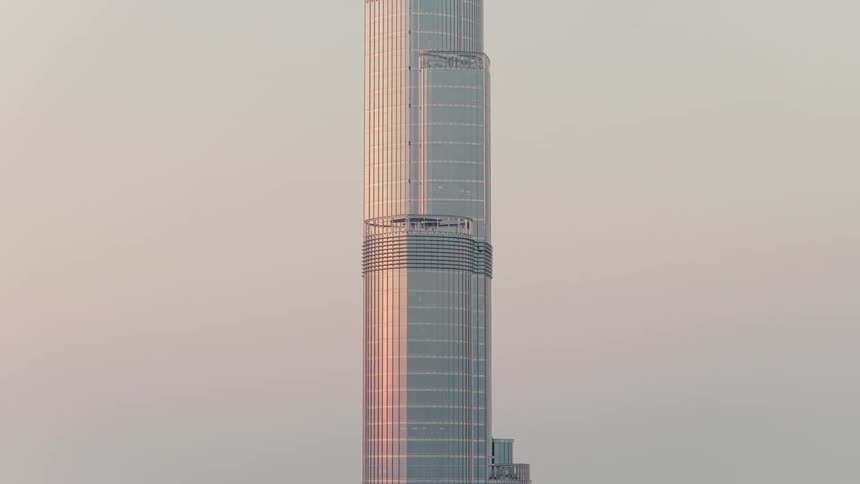 A close-up, slow zoom-out of the Burj Khalifa skyscraper as the sun reflects off its glass facade during a hazy sunset