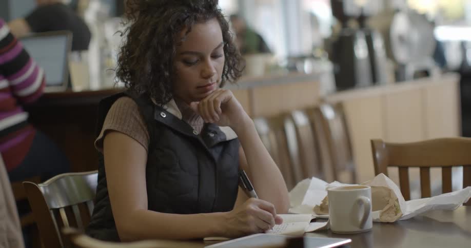 Woman sits at a table in a coffee shop writing in a notebook