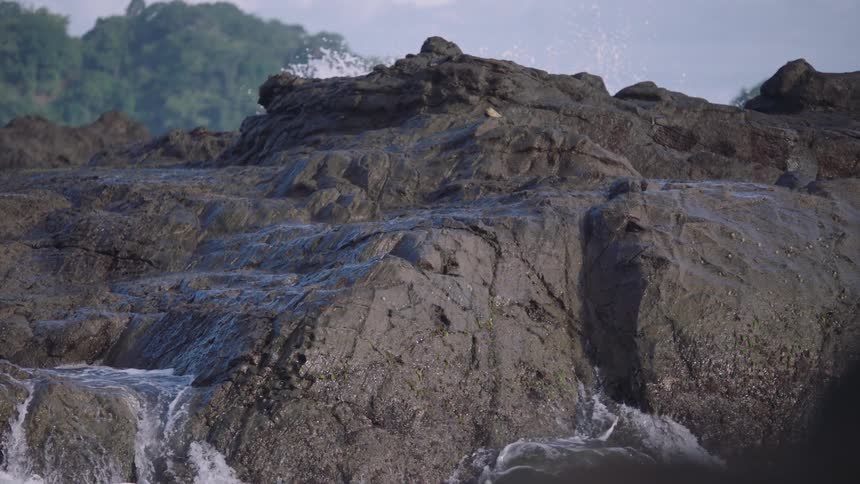 Slow motion close up of ocean water flowing over dark volcanic rocks on a tropical coastline