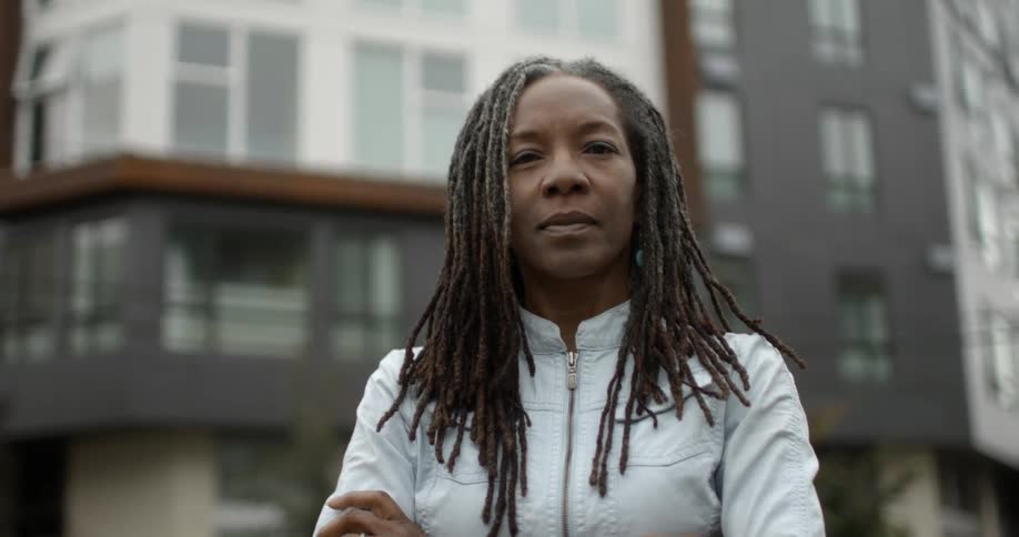 A woman is standing in an urban setting with her arms crossed