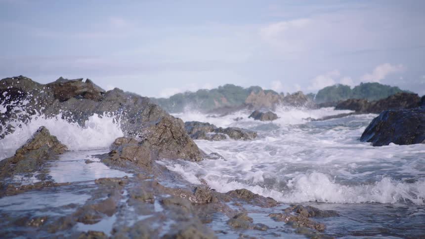Powerful ocean waves crash over a rugged tropical shoreline in dramatic slow motion