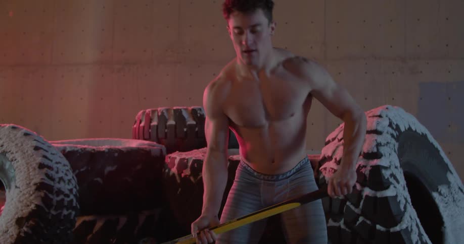 A man swinging a sledgehammer onto some big tires outside in the snow