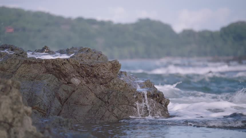 Dramatic slow motion close up of powerful ocean waves crashing against rugged rocks on the shore