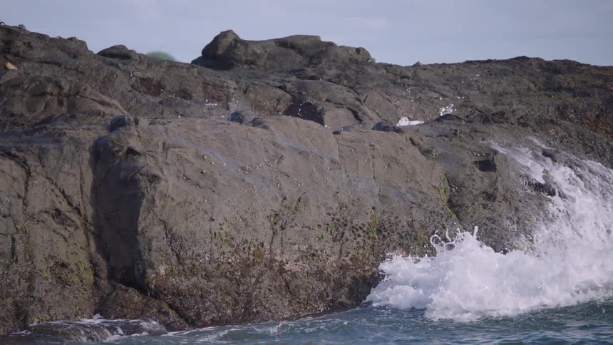 Dramatic slow motion of an ocean wave crashing against a large coastal rock