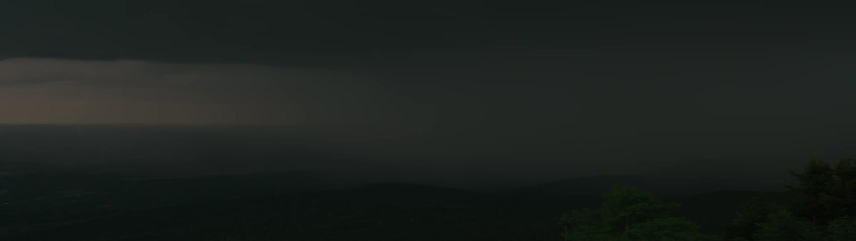 An intense thunderstorm with frequent lightning and loud thunder rages at night over a dark, hilly landscape