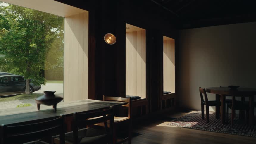 Interior view of a serene and modern home with dark wood walls and floors, where sunlight highlights built-in window seats