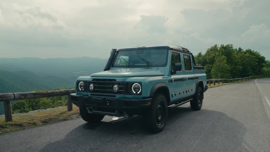 A modern off-road pickup truck is parked on a scenic mountain road overlooking a vast valley under a cloudy sky