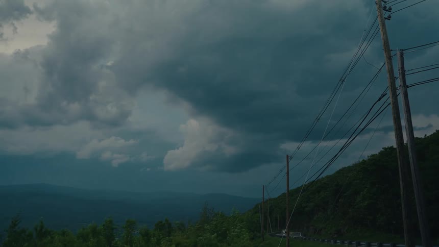 A dramatic time-lapse of dark, stormy clouds moving over a mountain valley road