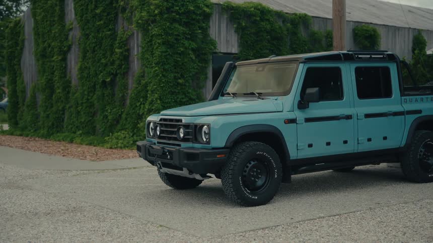A stylish light blue off-road pickup truck stands parked in front of an ivy-covered rustic barn