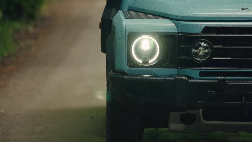 Atmospheric close-up of a rugged off-road vehicle's headlight shining as steam rises on a misty forest path